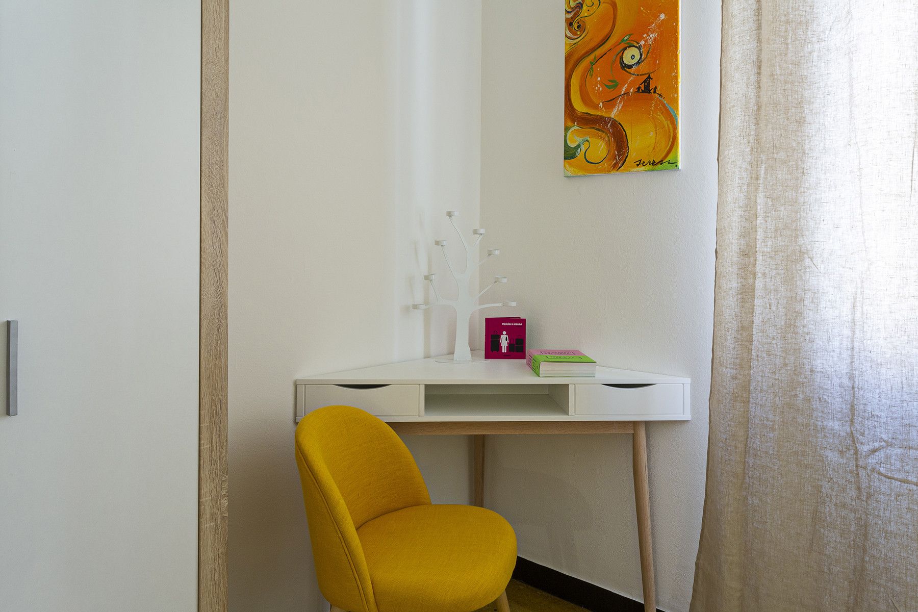 A room with a white desk, a yellow chair, a painting on the wall, and a door.