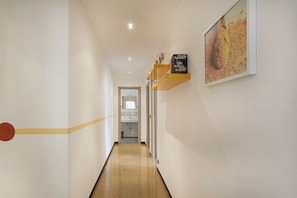 A hallway with a wooden floor, a white wall, and a framed picture on the right.