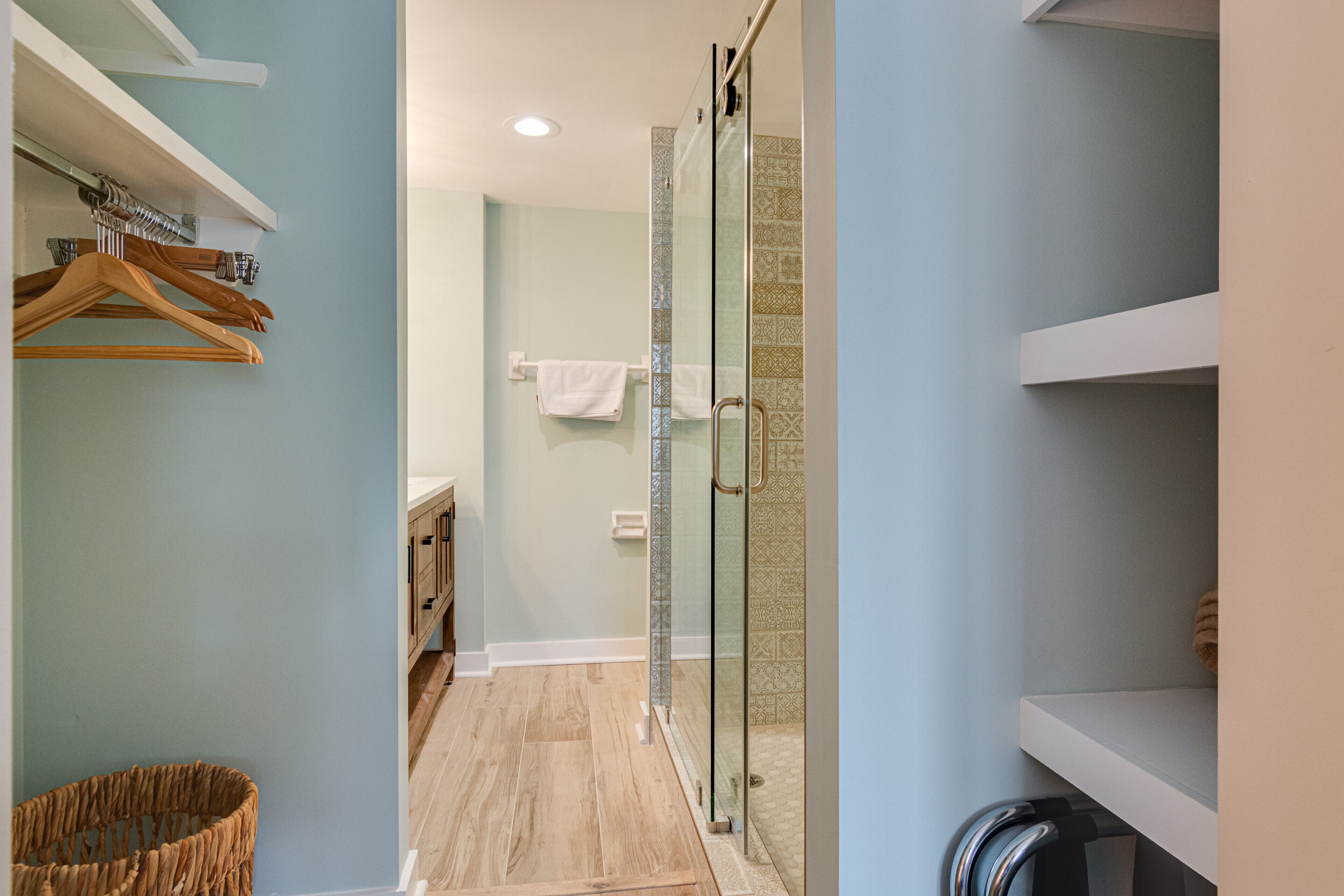 Un baño moderno con cabina de ducha de vidrio, perchas de madera en un perchero de pared y un toallero blanco.