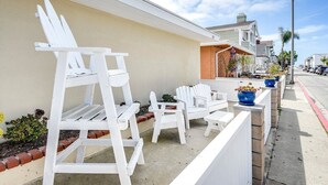 Una fila de sillas Adirondack blancas y una escalera en un patio de concreto junto a un edificio beige con base de ladrillo.
