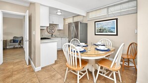 Cocina compacta con armarios blancos, refrigerador de acero inoxidable y un comedor con mesa redonda y sillas blancas.