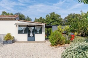 A modern house with a covered patio, a gravel driveway, and various plants.