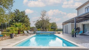 Una piscina rectangular con solárium alicatado, rodeada de sillones de descanso y plantas en macetas.