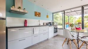 Una cocina moderna con armarios blancos, una campana extractora de acero inoxidable y un comedor con mesa y sillas de vidrio.