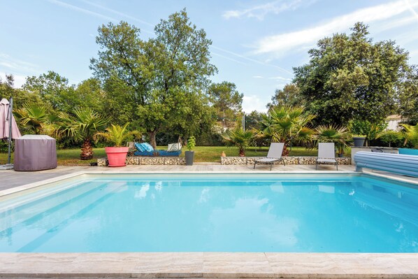 A swimming pool with lounge chairs and a covered seating area.