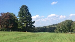 A golf course with a well-maintained green, a sand bunker, and a clear sky.