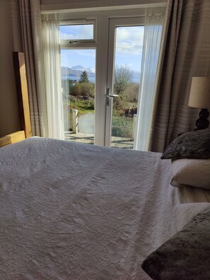 A bedroom with a bed, a view of mountains through a glass door, and a lamp on a bedside table.