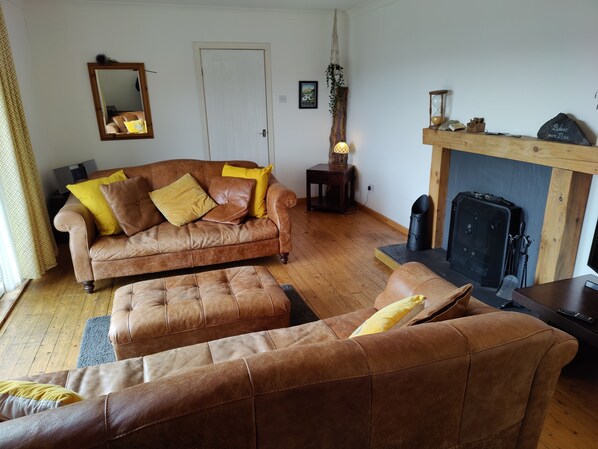 A living room with a brown leather sofa, a matching ottoman, and a wooden coffee table. There is a fireplace with a mantel, a mirror on the wall, and a small side table with a lamp.
