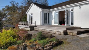 Un bâtiment blanc doté d’une terrasse en bois, d’un patio couvert et d’un chemin de pierre menant à l’entrée.