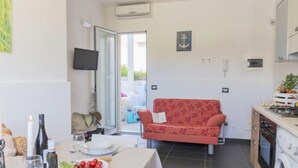 A compact living space with a dining area, a sofa, a kitchen with a washing machine, and a TV mounted on the wall. - Apartment Brezza by Interhome (Scicli)