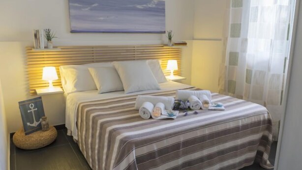 A neatly made bed with striped bedding, two bedside lamps, and a view of the sea through the window. - Apartment Brezza by Interhome (Scicli)