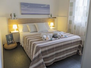 A neatly made bed with striped bedding, two bedside lamps, and a view of the sea through the window. - Apartment Brezza by Interhome (Scicli)