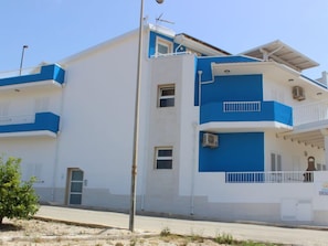A multi-story building with a white and blue exterior, balconies, and air conditioning units.