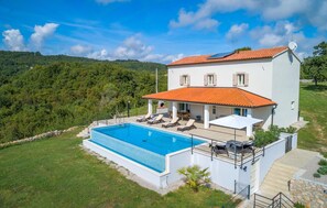 Ein zweistöckiges Haus mit Swimmingpool, einer Terrasse und Lounge-Möbeln sowie Blick auf die umliegenden Hügel.