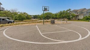 Una cancha de baloncesto al aire libre con un aro, rodeada de árboles y edificios residenciales.