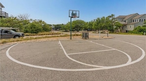 An outdoor basketball court with a hoop, surrounded by trees and residential buildings.