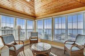 Une pièce meublée de mobilier en osier, avec une table ronde et de grandes fenêtres équipées de stores.