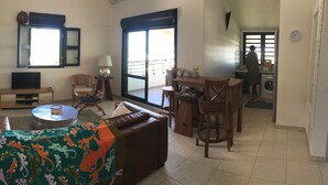 Ein Wohnzimmer mit einer Couch, Sesseln, einem Fernseher und einem Essbereich mit Tisch und Stühlen.