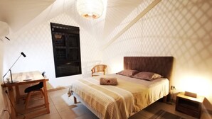 Ein Schlafzimmer mit Bett, Schreibtisch und Stuhl. Ein Fenster mit Jalousien, eine Lampe und ein Teppichboden sind ebenfalls vorhanden.