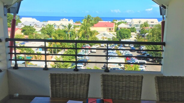 Ein Balkon mit Korbstühlen und einem Tisch, der auf einen Parkplatz und Gebäude mit Meerblick blickt.