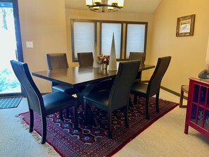Un comedor con una mesa rectangular rodeada por seis sillas, un candelabro arriba y una ventana con persianas.