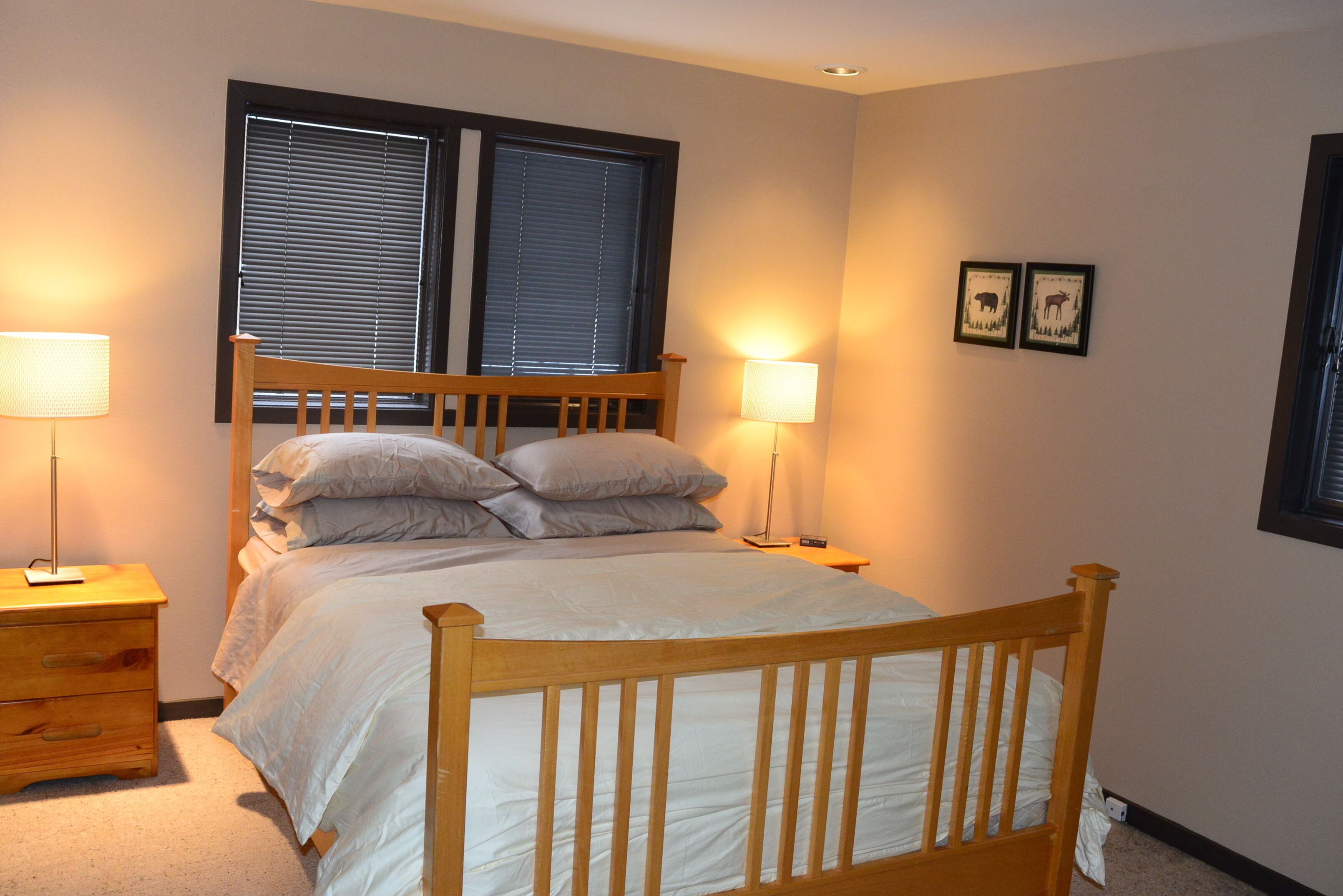 A neatly made bed with a wooden headboard, two bedside lamps, and a window with blinds.