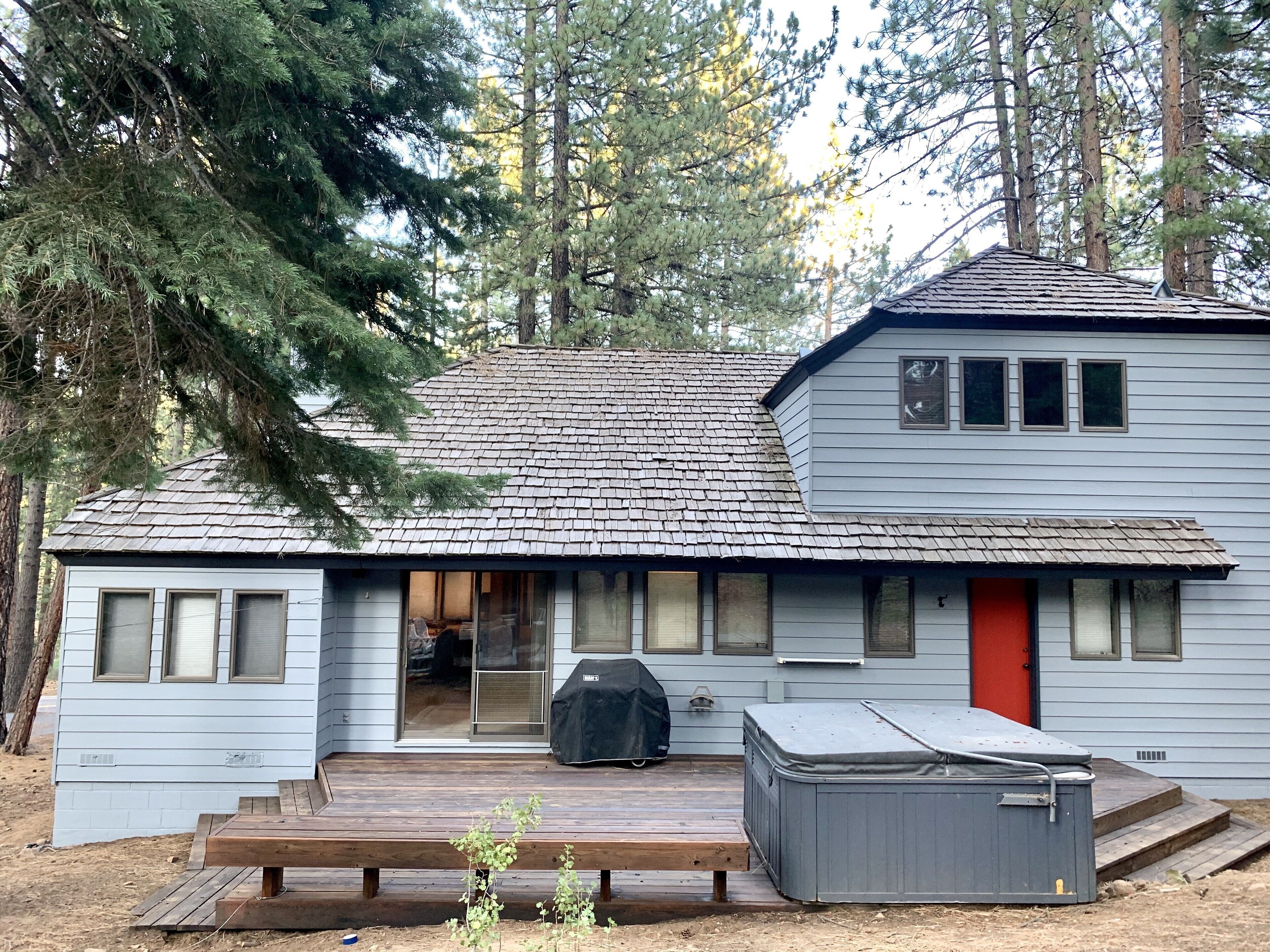 Une cabane à deux étages dotée d’une terrasse couverte, d’une porte rouge et d’un jacuzzi.