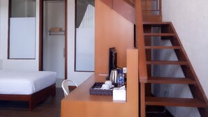 A modern hotel room with a wooden staircase, a bed, a desk with a kettle, cups, and a bottle. - Pondokan Tjiburial (Bandung)