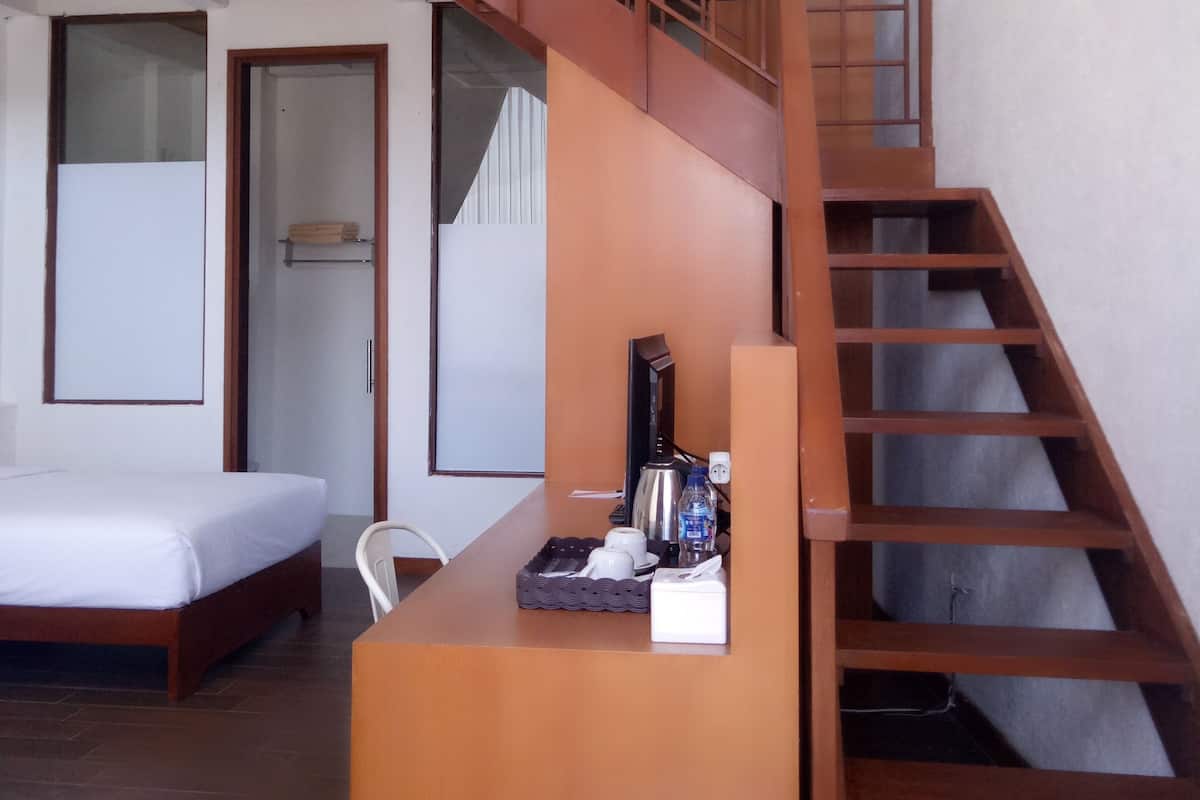 A modern hotel room with a wooden staircase, a bed, a desk with a kettle, cups, and a bottle.