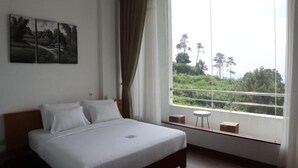 A bedroom with a large bed, a small table, and a window with a view of greenery. - Pondokan Tjiburial (Bandung)