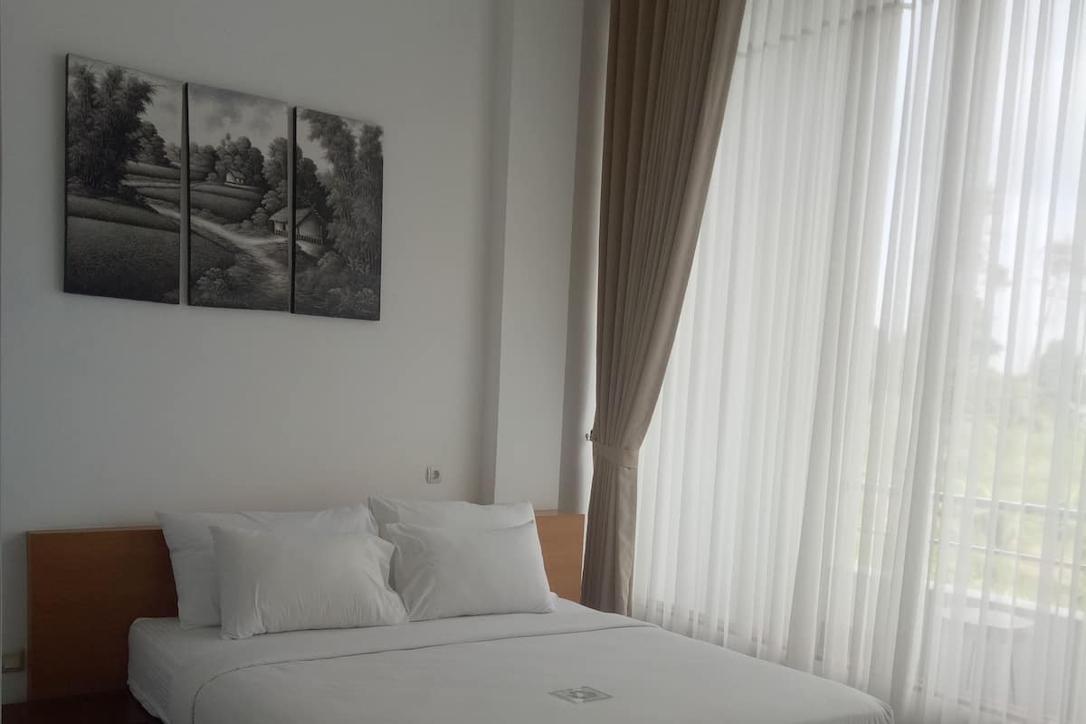 A neatly made bed with white linens, a wooden headboard, and a set of three landscape paintings on the wall.