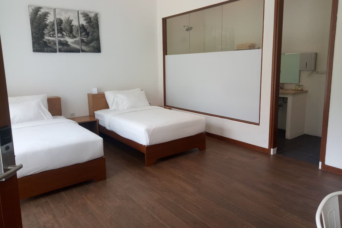 A hotel room with two single beds, a wooden floor, a large mirror, and a painting on the wall.