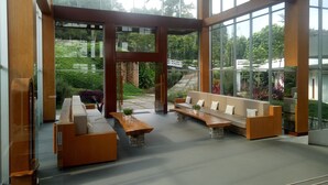 A spacious indoor area with large windows, wooden furniture, and a view of a garden. - Pondokan Tjiburial (Bandung)