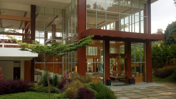 A modern building with large glass windows, a covered entrance, and a stone pathway leading to the entrance. - Pondokan Tjiburial (Bandung)