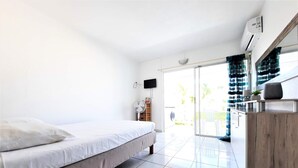 Ein modernes Schlafzimmer mit Bett, Fernseher, Ventilator und einer Schiebeglastür, die auf einen Balkon führt.