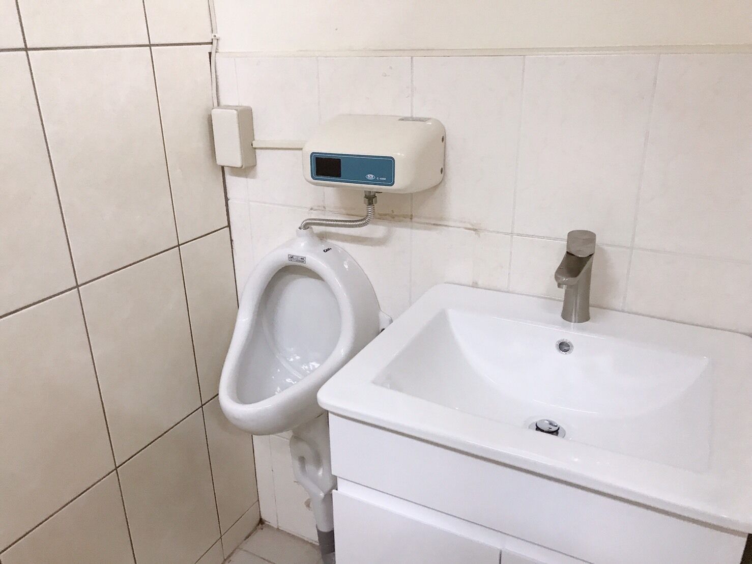 Ein Urinal neben einem Waschbecken, darüber ein digitales Display.