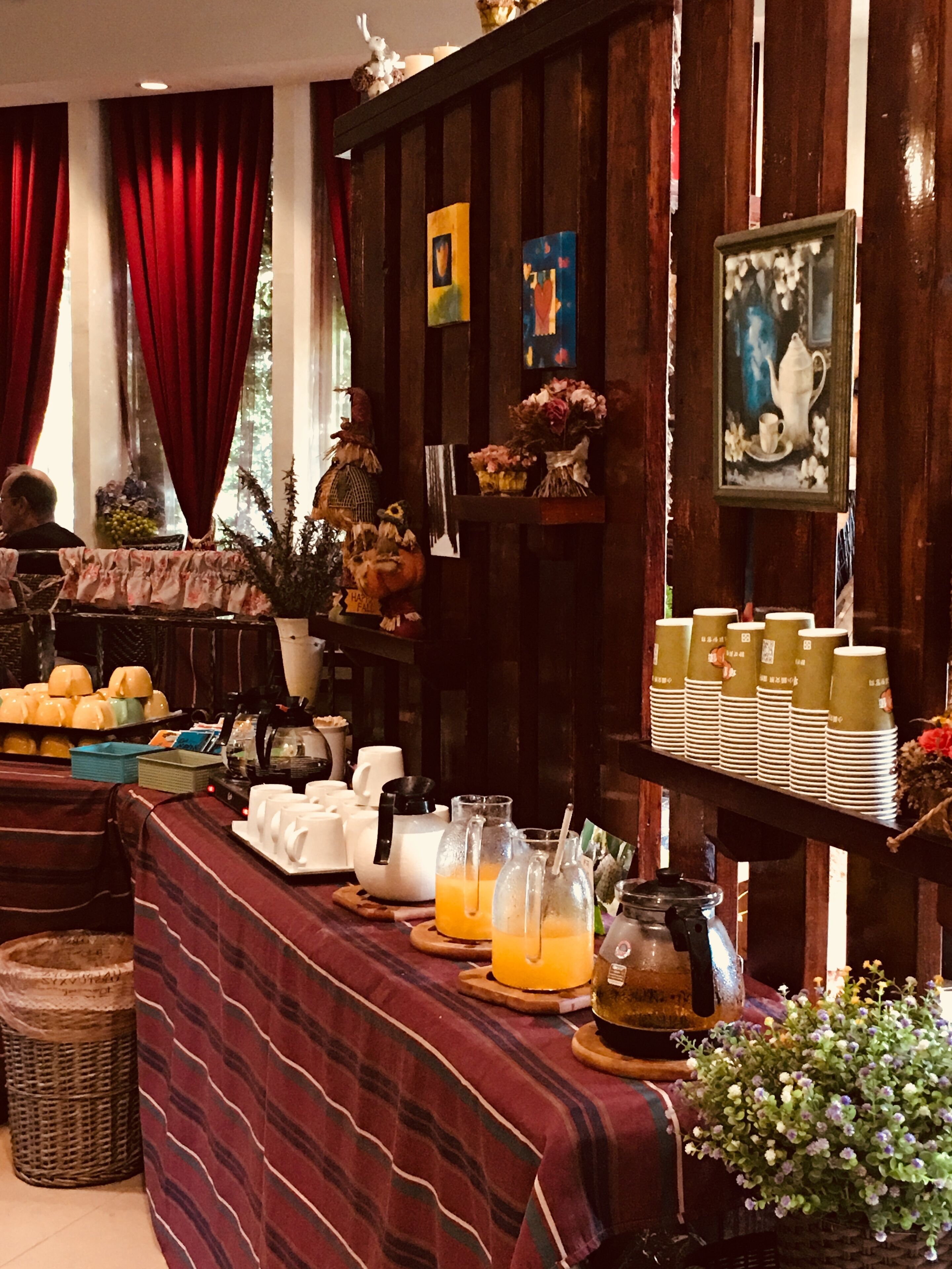 Montaje de bufé con diversas opciones de comida y bebidas, una estación de café y elementos decorativos como flores y obras de arte en las paredes.