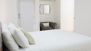 Ein Schlafzimmer mit Bett, Kissen, einem Sessel, einer Tür und einem Spiegel.