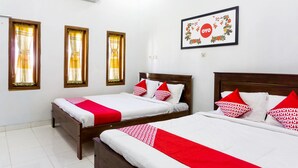 A hotel room with two beds, each with white bedding and red accents, a framed floral artwork on the wall, and an air conditioning unit above the beds.