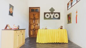 A room with a wooden door, a yellow table with a cloth, and a wall-mounted sign reading "OYO".