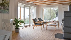 Quarto espaçoso com piso de madeira, grandes janelas e vista para o exterior. Há duas cadeiras e uma mesa pequena.