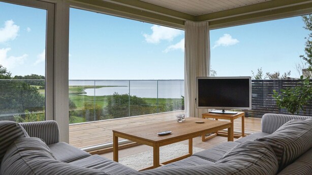 Varanda espaçosa com mesa e sofá de madeira, televisão de tela plana e vista para um lago.