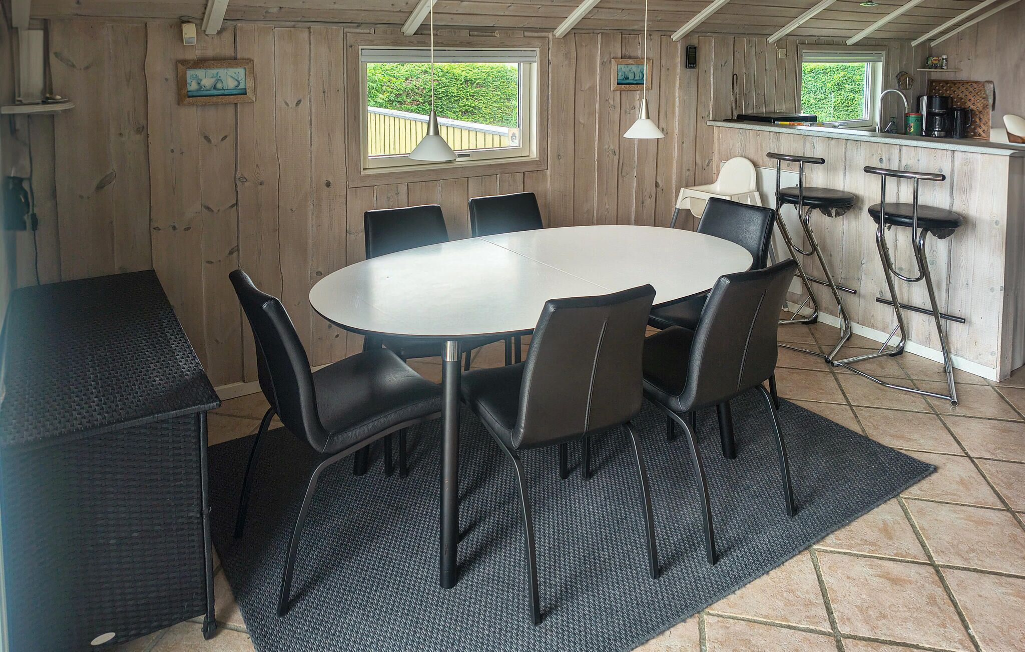 Een eetgedeelte met een ronde tafel en stoelen, een bar met krukken, en houten wanden.