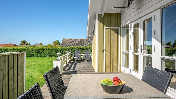 A balcony with outdoor furniture, a bowl of fruit, and a view of a house with a tiled roof. - 3 bedroom amazing home in Haderslev (Haderslev)