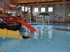 Una piscina interior con un tobogán con temática náutica, una fuente de agua y un aro de baloncesto.