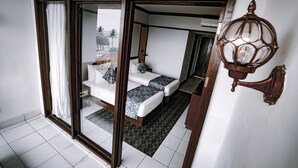 Quarto com uma grande janela, uma cama com colcha estampada e um abajur decorativo na parede.
