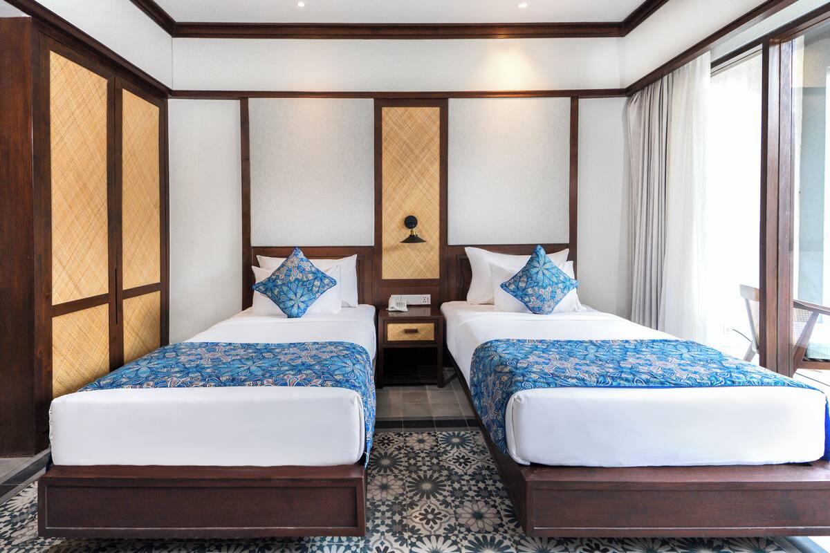 A hotel room with two beds, a nightstand, and a large window.