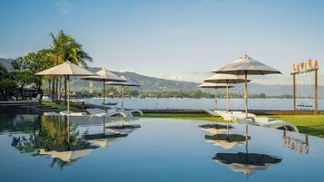 An infinity pool with lounge chairs and umbrellas, a view of the lake, and a sign with the name 'LOVINA'.