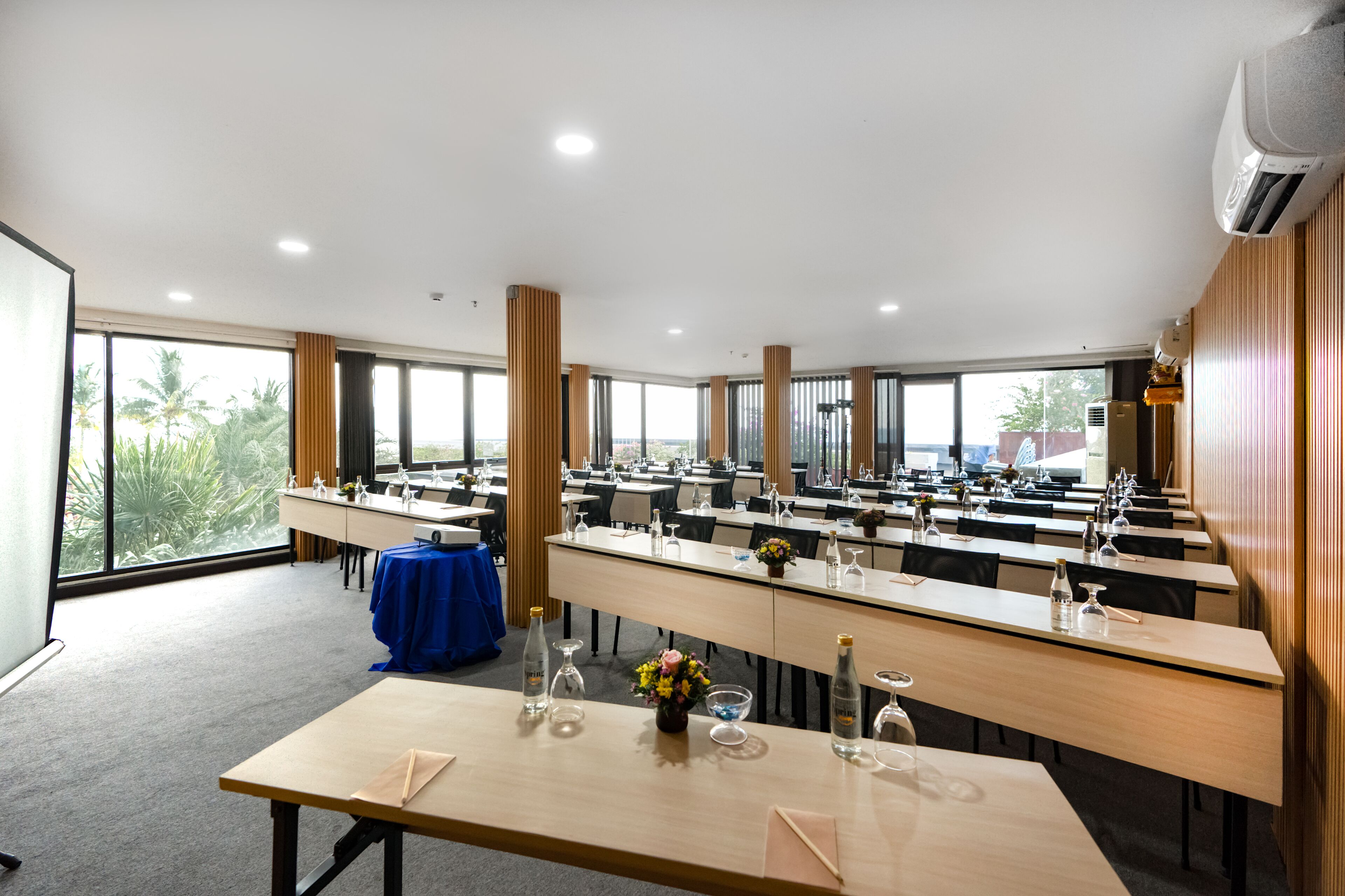 Un salón de conferencias con varias mesas, sillas y un amplio ventanal que ofrece vistas a palmeras.
