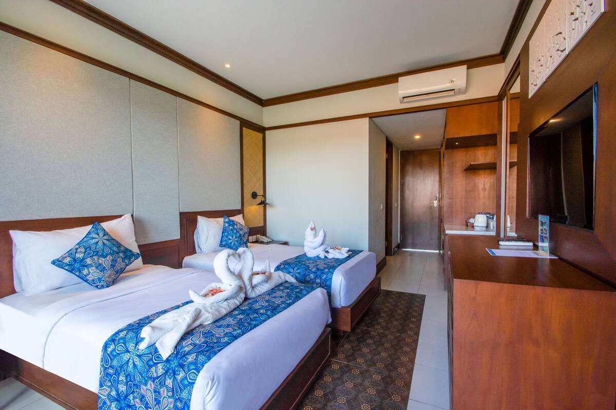 A hotel room with two beds, a wooden headboard, a TV, and a reception desk.